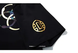 Détail de l'écusson doré et du lettrage coloré UGEJIA sur un t-shirt noir en coton épais