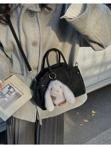 Detailed view of a black leather crossbody bag with a cute white plush bunny charm