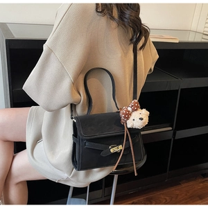 Detail of black suede shoulder bag featuring a metal twist lock and cute bear charm