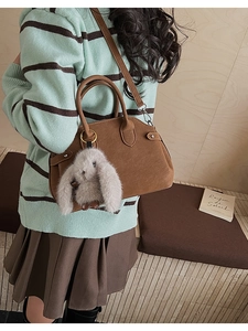 Close-up of brown matte leather handbag with a cute plush bunny charm and striped sweater