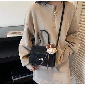 Detail of black Kelly style bag with plush bear charm worn with beige ribbed outfit