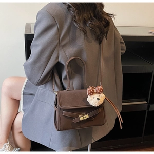 Detail view of dark brown leather shoulder bag with cute plush bear and bow charm