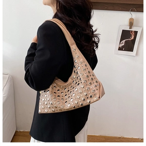 Sac seau beige à rivets argentés avec large bandoulière porté par un mannequin