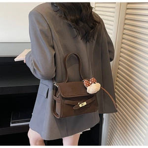 Detail of dark brown suede shoulder bag with gold clasp and plush puppy charm