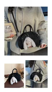 Detail of black suede baguette bag with cute grey plush rabbit charm and shoulder strap