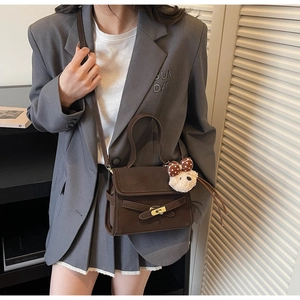 Detail of a brown crossbody bag with gold buckle and a cute teddy bear charm on the strap