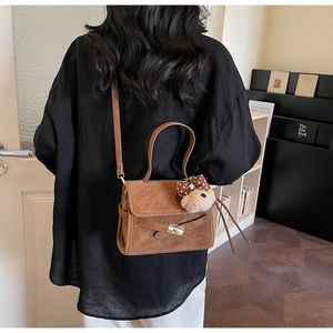 Detail view of brown suede handbag with gold lock and cute plush bear charm on strap