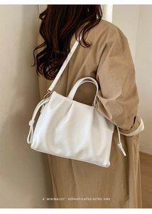 Sac fourre-tout blanc plissé minimaliste avec poignée et bandoulière porté sur un trench