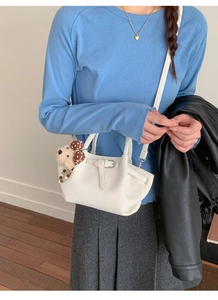 Close-up of white pleated bucket bag with cute bear charm and drawstring detail