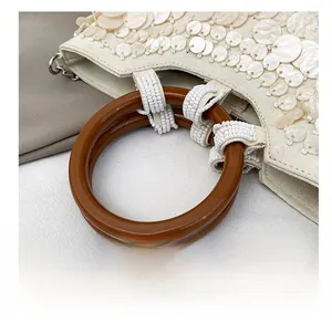 Detail of amber resin handle and shimmering sequins on a cream crossbody handbag