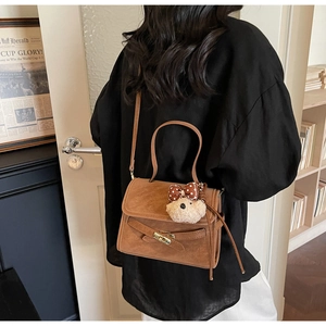 Close-up of retro brown shoulder bag with a teddy bear charm on a model's arm