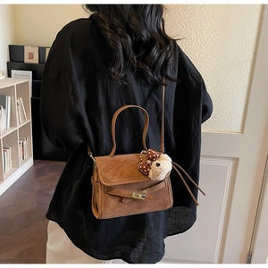 Rear view of model carrying a vintage brown leather shoulder bag with a cute plush bear charm