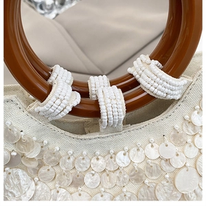 Close-up of mother-of-pearl sequins on off-white canvas with round brown handle