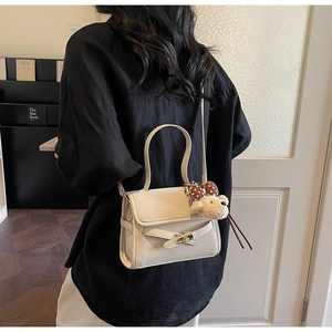 Cream shoulder bag shown on model with a cute brown plush bear charm detail