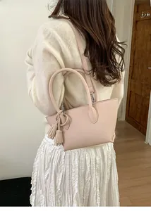 Detail of pink leather bucket bag with dual tassels worn by a model in a casual setting