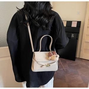 Detail view of cream shoulder bag with rotary lock and cute brown polka dot bear charm