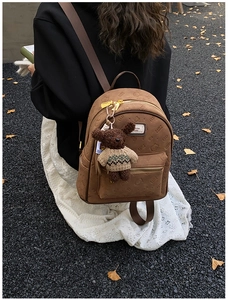 Nahaufnahme des braunen Rucksacks mit Kitty-Prägung und Bärenanhänger im Herbstdekor