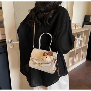 Detailed view of beige shoulder bag with gold hardware and a cute plush bear charm