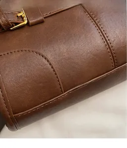Detail of brown lychee-textured faux leather bag with stitching and gold buckle