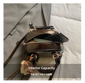 Detail showing inner capacity of a brown glossy leather handbag with teddy bear charm
