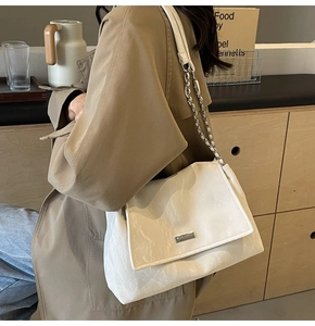 Dettaglio borsa a patta in pelle bianca con tracolla a catena su un cappotto marrone