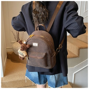 Detail eines dunkelbraunen Rucksacks mit Bärenanhänger und Vintage-Markenetikett am Modell