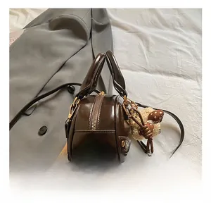 Detail of dark brown glossy Boston bag featuring gold hardware and a cute plush charm