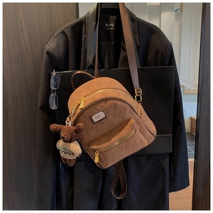 Detail eines braun geprägten Mini-Rucksacks mit Plüschbären-Anhänger auf dunklem Sakko
