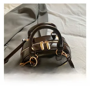 Detailed shot of dark brown patent leather mini boston bag with golden zippers and bear charm