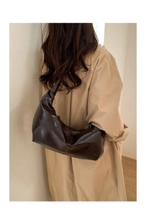 Model wearing a dark brown glossy leather hobo bag with a crescent shape and zip closure