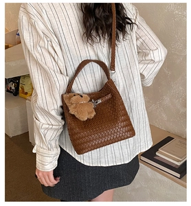 Detail of woven texture on dark brown bucket bag with plush bear charm and silver lock
