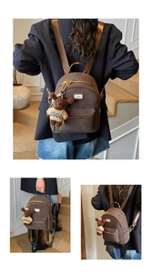 Detail eines dunkelbraunen Rucksacks mit Bärenprägung, Metalllogo und Plüschtier