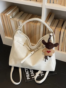 White lychee pattern leather tote bag with a cute bear charm on a white bookshelf