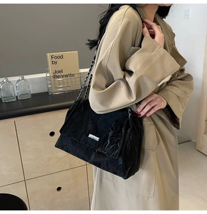 Dettaglio borsa tote nera stropicciata con catena d'argento indossata su cappotto beige