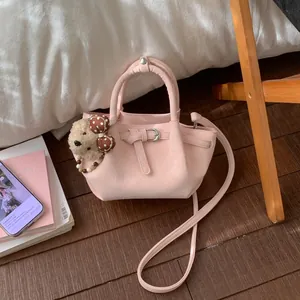 Détail du sac seau plissé rose avec pendentif ours sur un parquet en bois