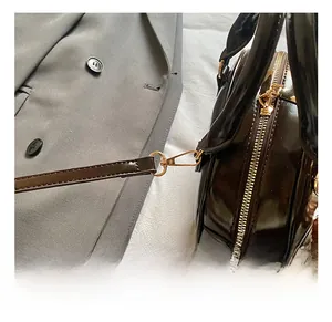 Detail of dark brown patent leather handbag with gold metal hook and zipper closure