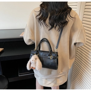 Rear view of minimalist black leather crossbody bag with cute beige rabbit charm