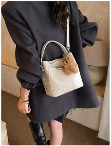 Detail of white woven bucket bag featuring silver lock and brown plush bear charm