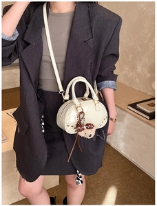 White mini bowling bag with plush bear charm and golden hardware on grey suit model