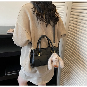 Detail of black PU crossbody bag with golden buckle and grey plush rabbit charm decoration