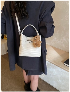 Detail of white woven bucket bag with silver metal clasp and plush bear charm