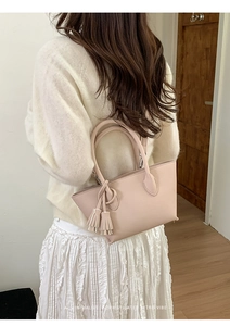 Detailed side view of a light pink bucket bag with tassel charm and round top handle