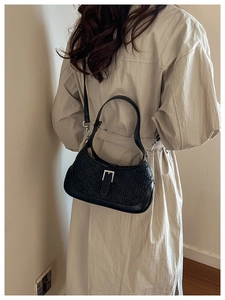 Close-up of black textured leather shoulder bag with silver buckle on a trench coat