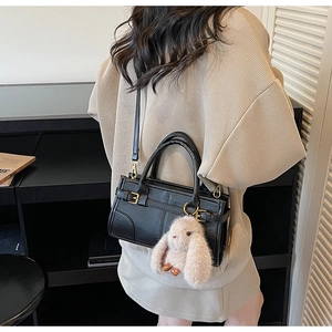 Close-up of black leather crossbody bag featuring a soft brown plush rabbit keychain charm