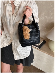 Close-up of black woven bucket bag texture with a cute brown plush bear pendant detail