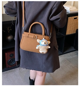 Detail of brown litchi grain leather handbag with cute bear charm worn on dark coat