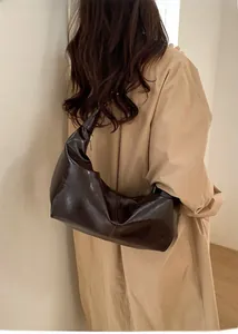 Detail of a dark brown glossy leather hobo bag with zipper and minimalist shoulder strap