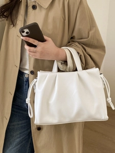 Sac cabas plissé blanc minimaliste avec cordon de serrage porté par un mannequin en trench