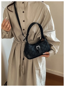 Close-up of a black quilted hobo bag with silver buckle detail on a beige shirt dress