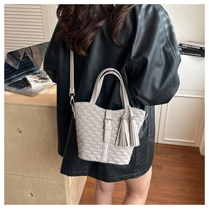 Detail of beige pleated bucket bag with tassel charms and shoulder strap in street style
